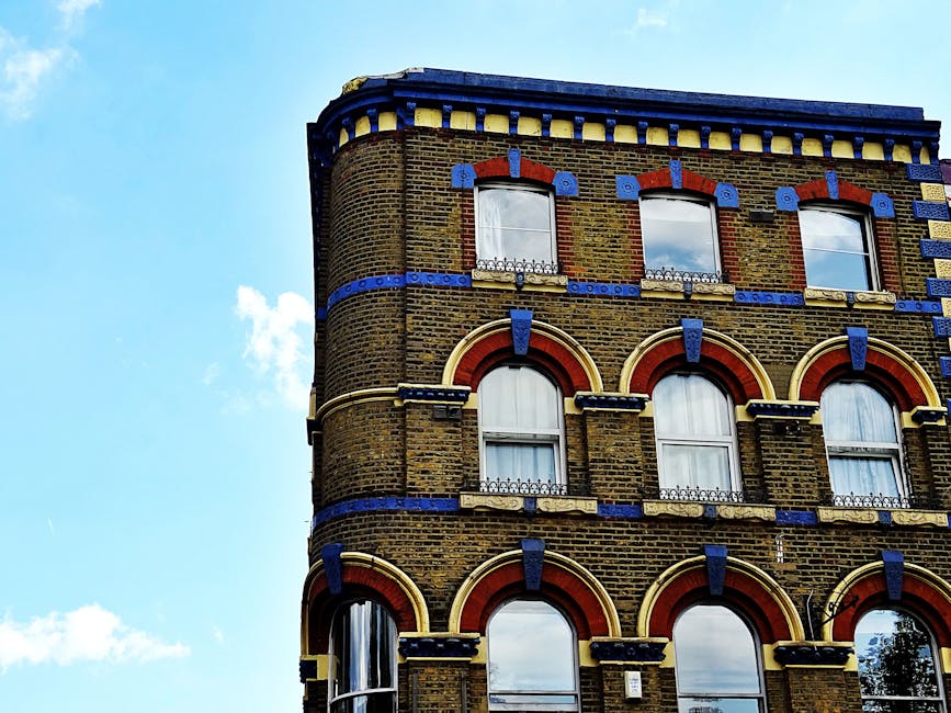 A silver and white commercial van from Man and Van Haringey is parked on a city street in front of a multi-storey brick building with large windows, during daylight hours with overcast skies. The van 