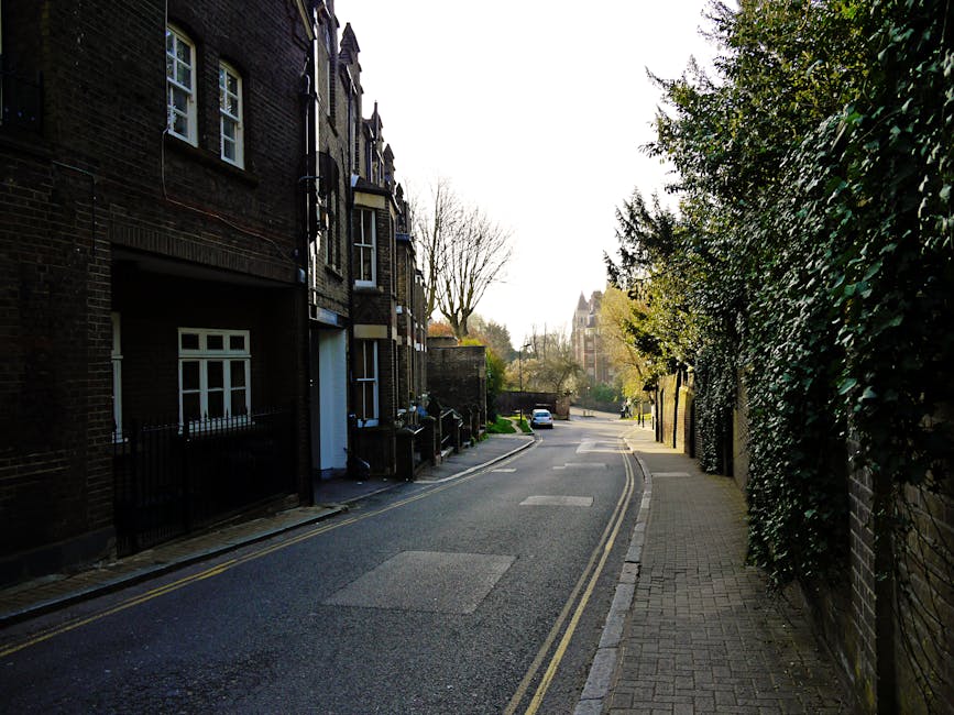 A narrow residential street in Crouch End, Haringey, with brick terraced houses on the left side, each featuring white-framed windows and small front gardens enclosed by black metal fences. The street